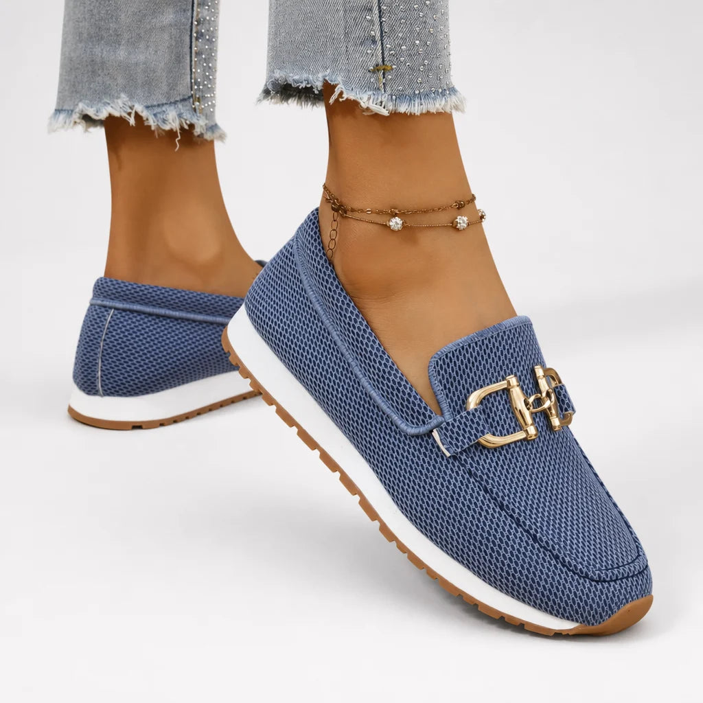 Blue mesh loafers with gold buckles worn by a model against a clean white studio backdrop.