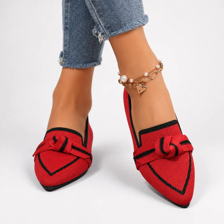 Red pointed flats with black trim worn by a model in a bright studio.