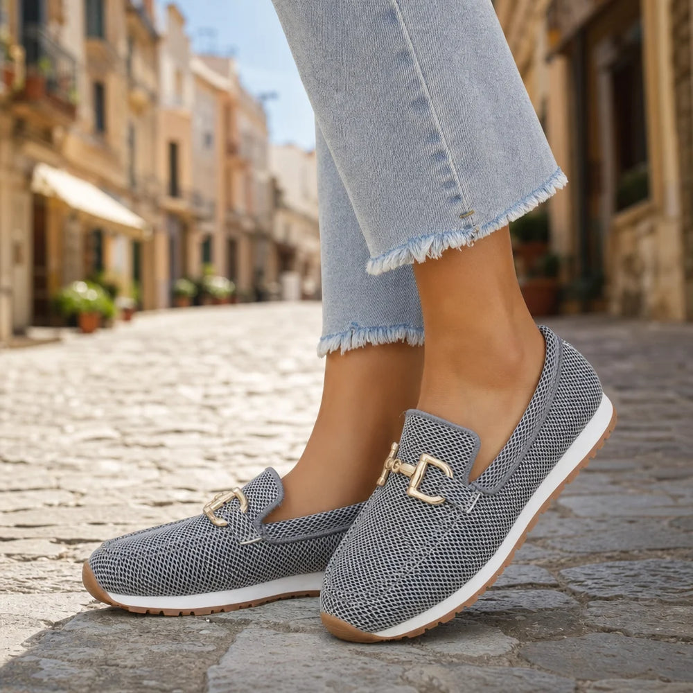 Gray mesh loafers with gold buckles worn outdoors on a sunny Italian street.