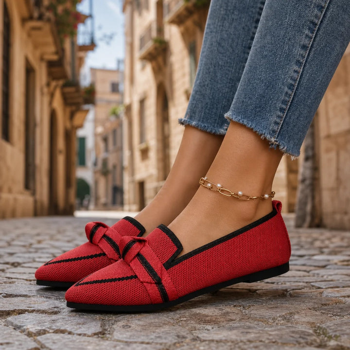 Red pointed loafers with black trim worn on a sunny Italian street.