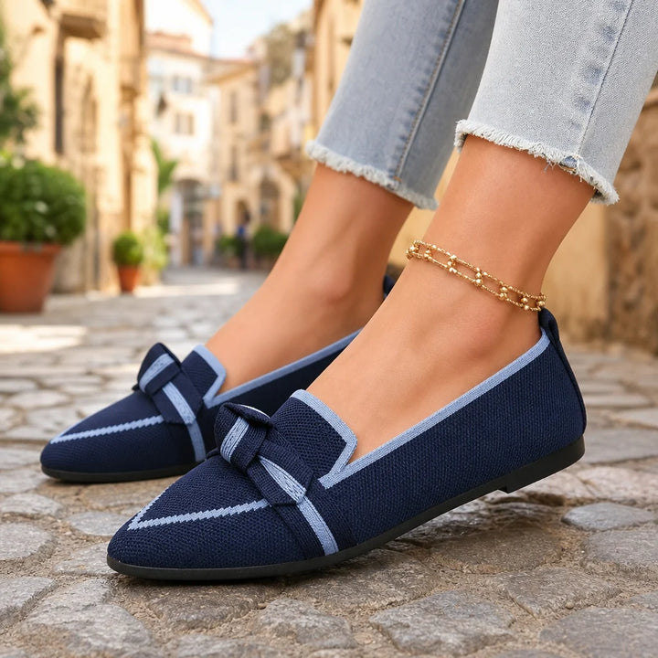 Navy blue bow loafers with light trim worn on a sunlit Italian street.