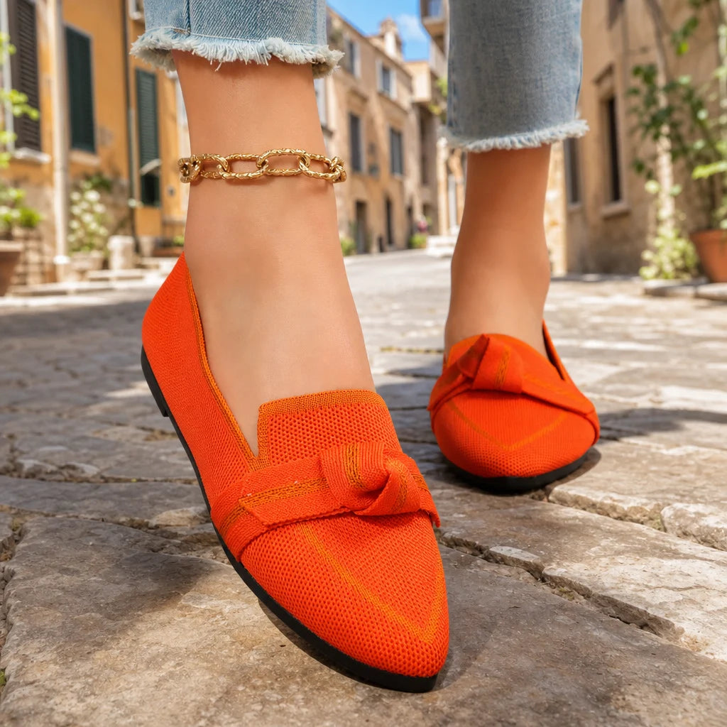 Bright orange bow loafers worn on feet in a sunny Italian street.