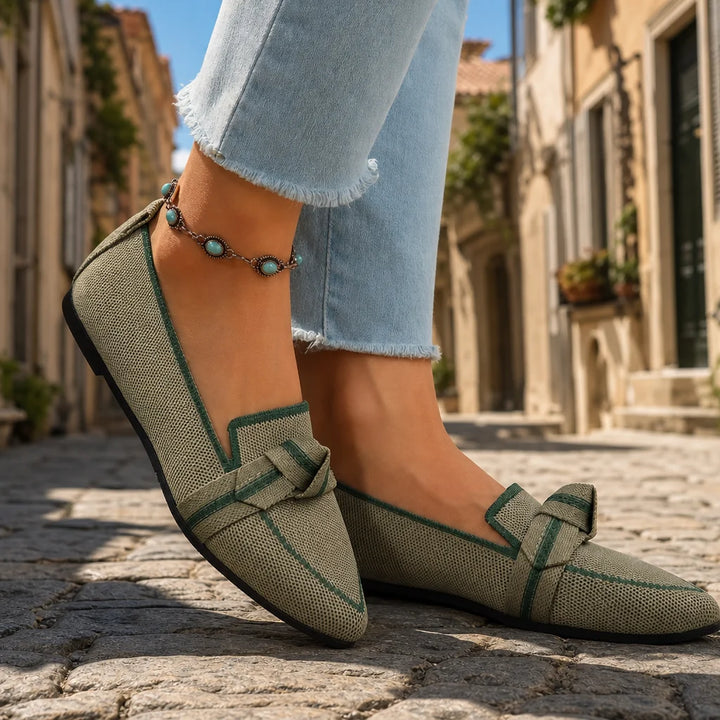 Olive woven loafers with green trim and bow worn with cropped jeans on a sunny Italian street.