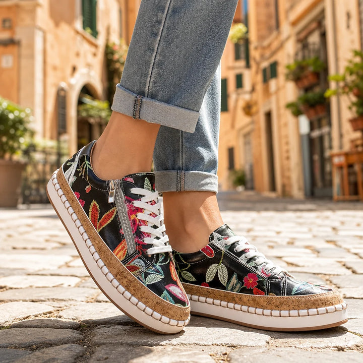 Black floral sneakers with cork midsoles and white laces worn on a sunny Italian street.