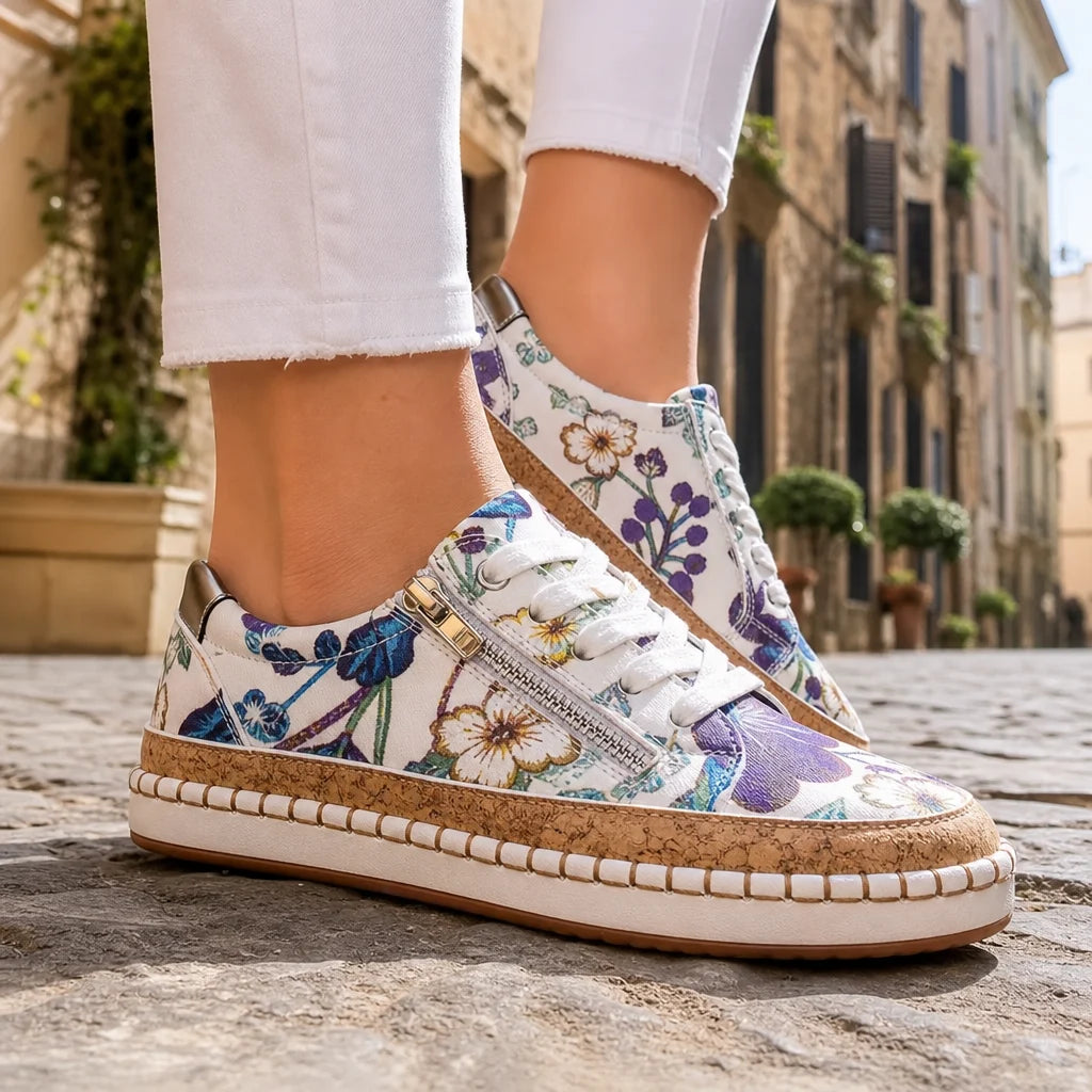 Floral white sneakers with cork trim and white laces worn on a sunny Italian street.