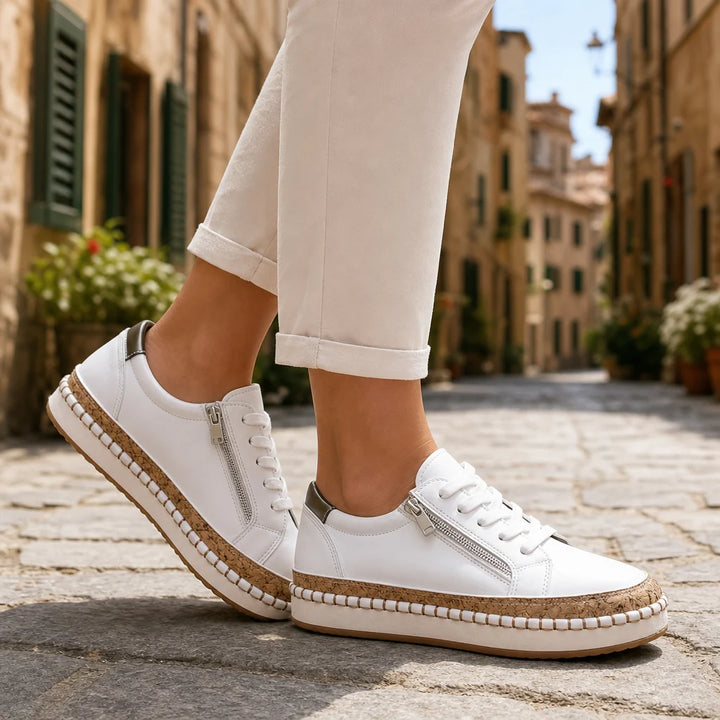 White leather zip sneakers with cork trim worn on a sunny Italian street.