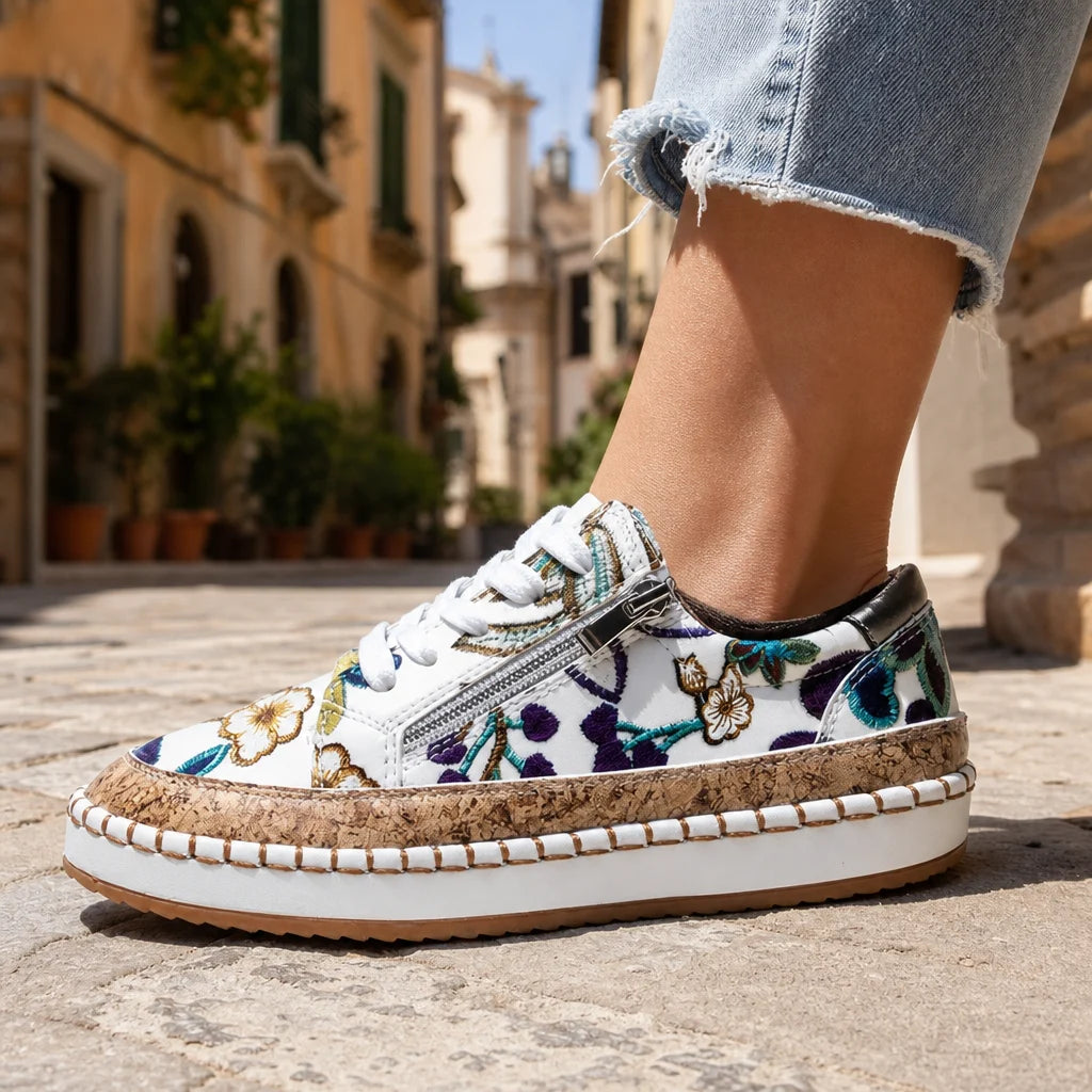 Floral low-top sneaker with cork platform sole and side zipper worn on a sunny Italian street.